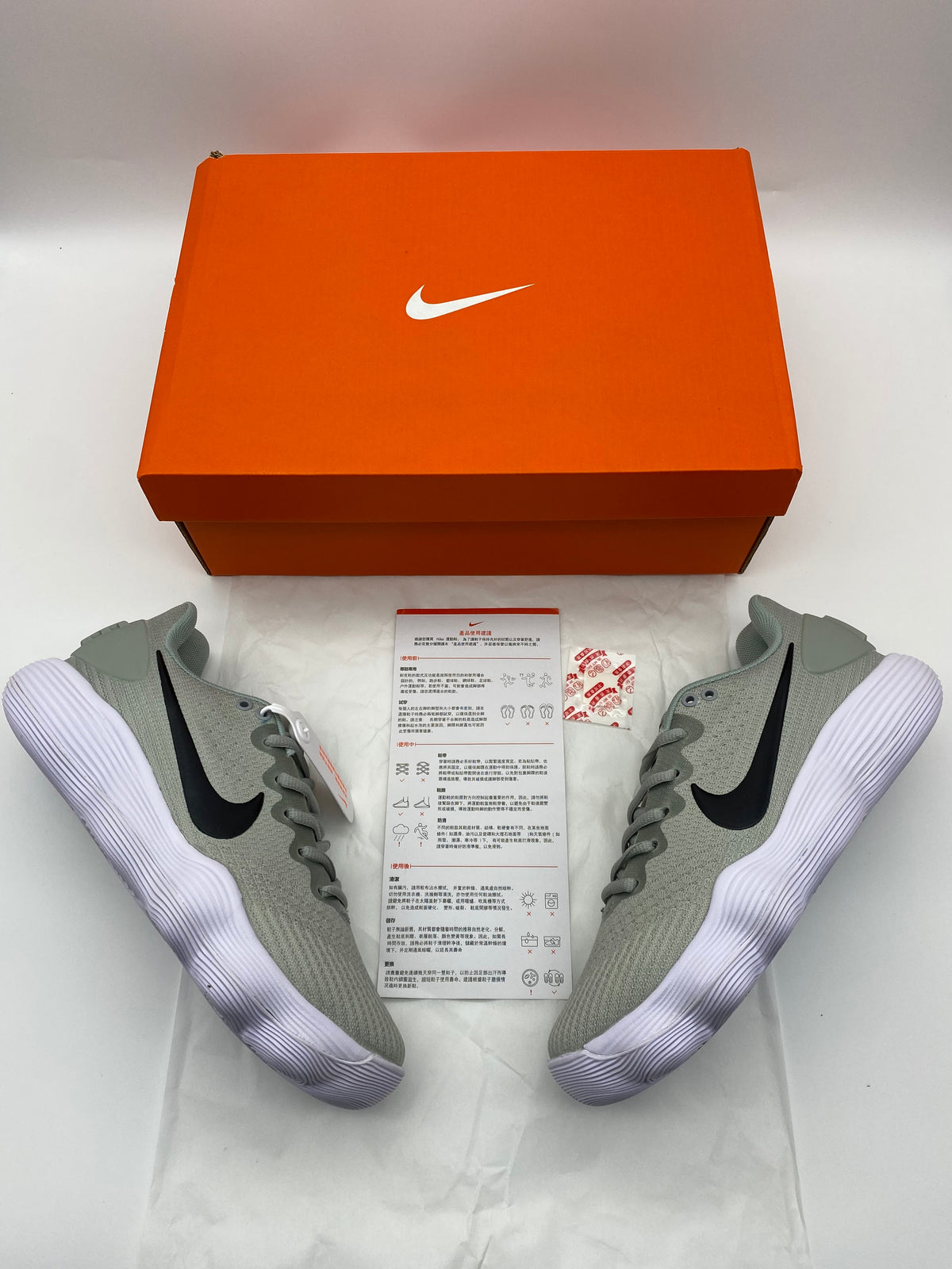 Grey Nike sneakers with black Swoosh logos and white ridged soles beside an orange shoe box