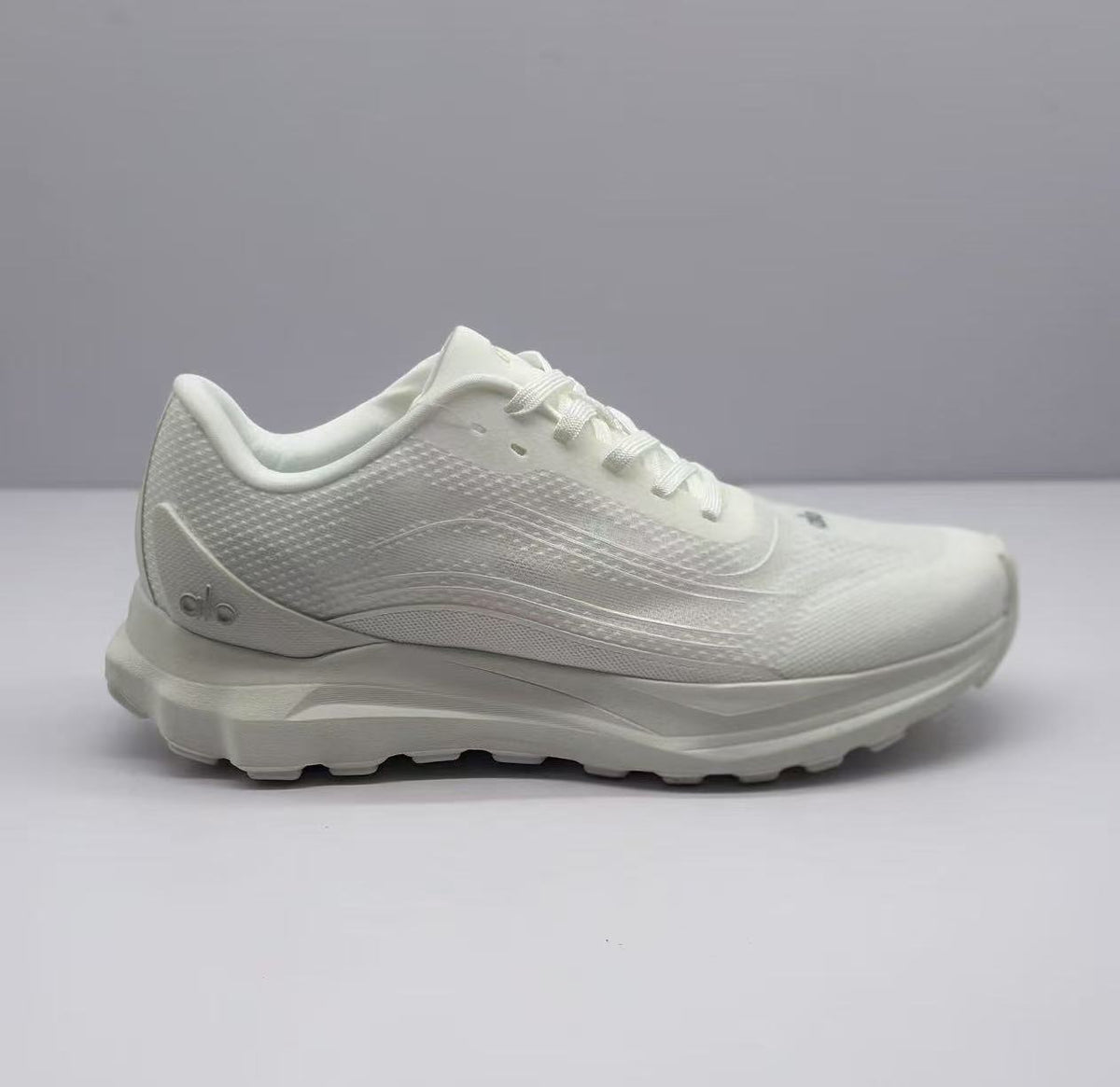 Side view of an all-white Alo low-top sneaker with a textured upper and layered sole.