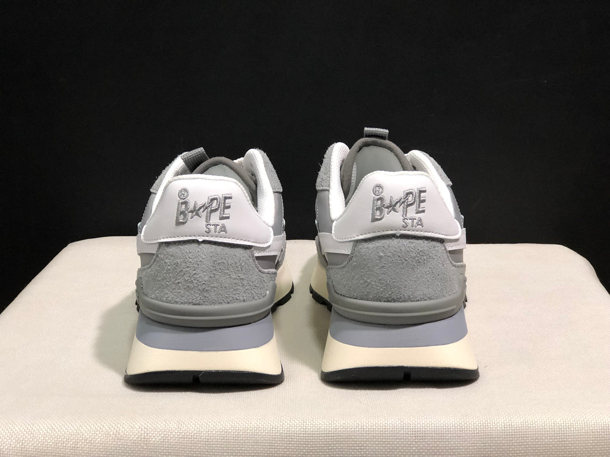 Rear view of the grey sneakers showing BAPE STA heel branding, padded collars, cream midsoles, and black outsoles.