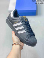 Angled side view of the black sneaker showing the Superstar side label, white stripes, and shell toe.