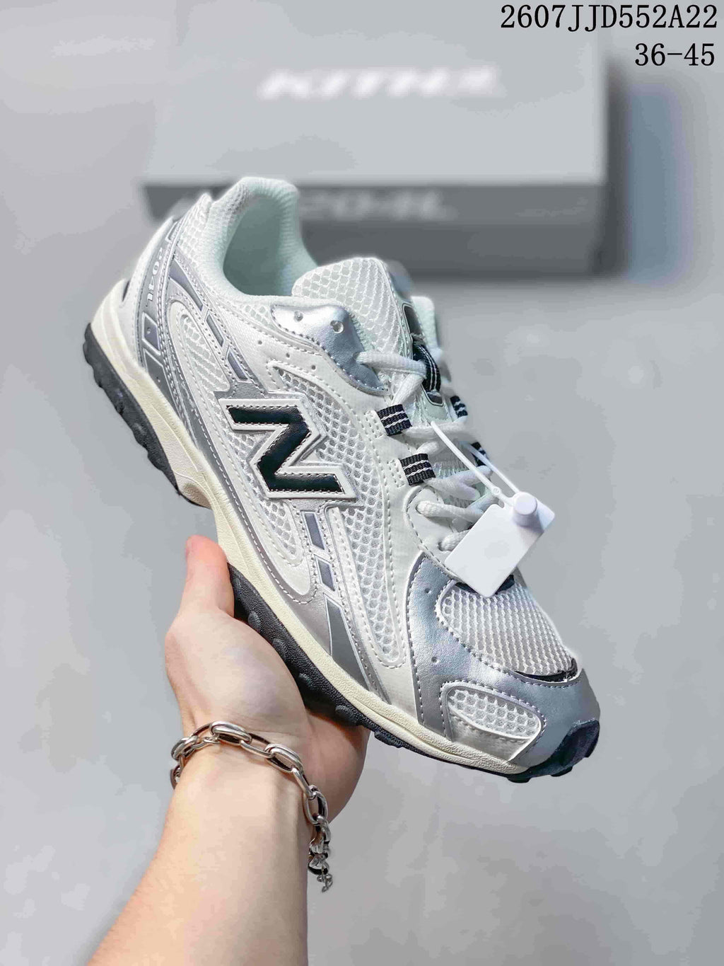 Three-quarter side view of the white and silver sneaker showing the layered upper, dark side logo, lace-up design, and black outsole.