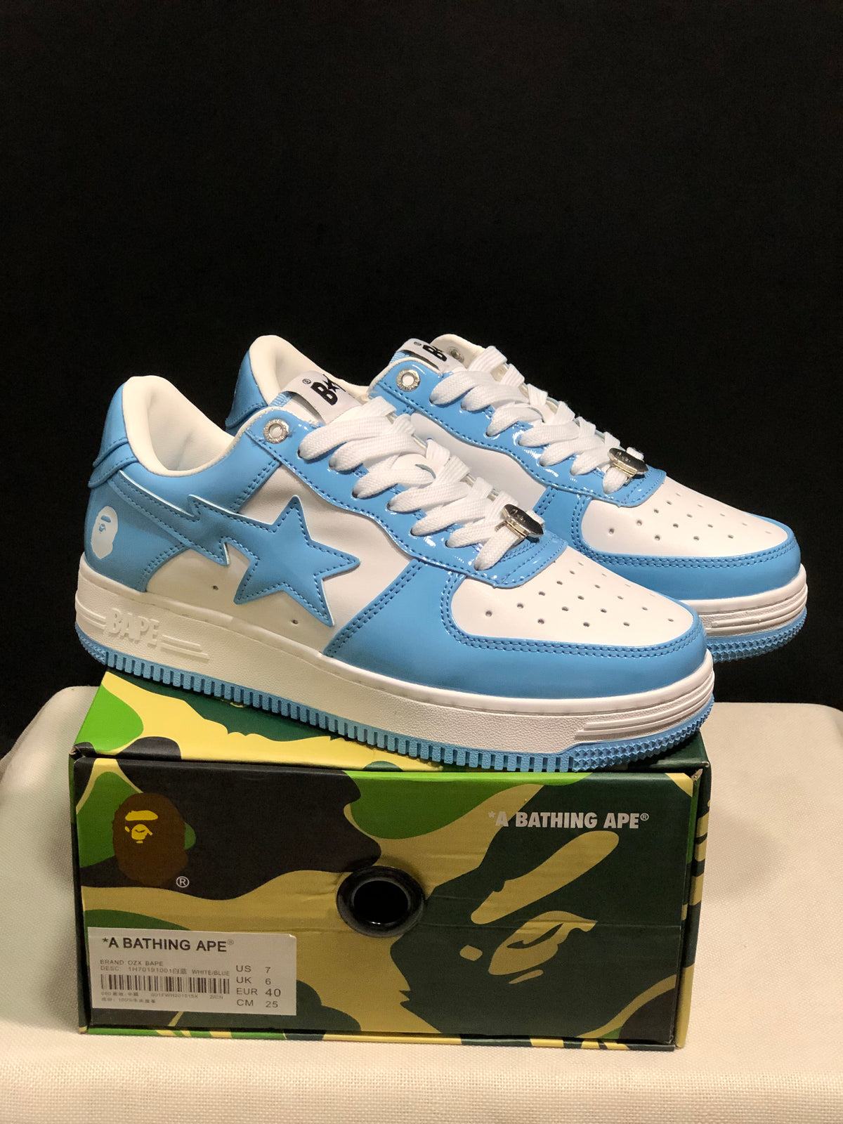 Blue and white BAPE STA low-top sneakers displayed on a camouflage shoebox; the box label shows US 7, EUR 40, and CM 25.