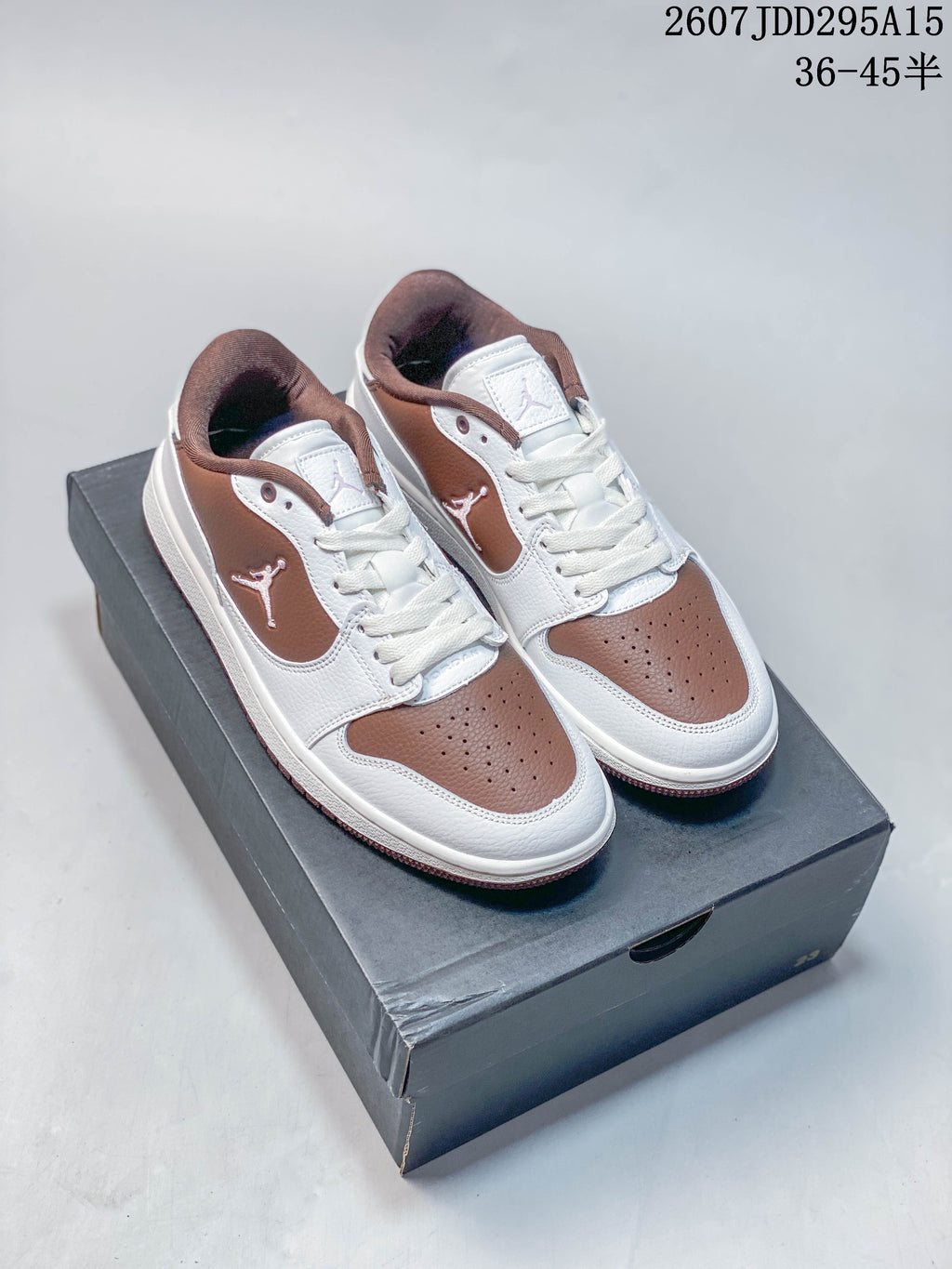 Pair of white and brown Jordan low-top sneakers displayed on a black shoe box.