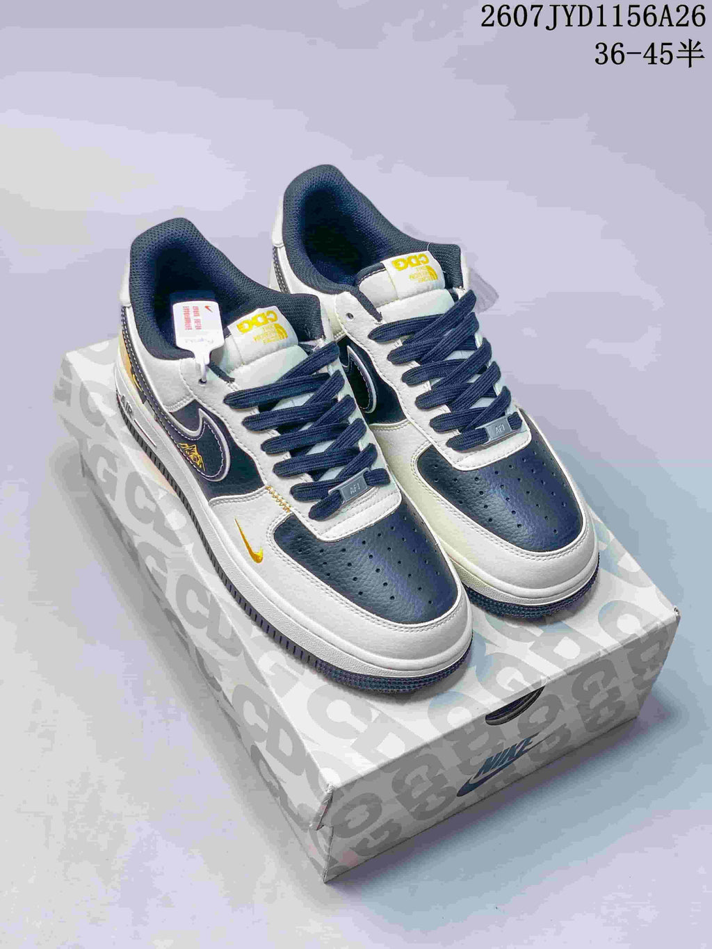 Pair of white, navy, and yellow Nike Air Force 1 low-top sneakers displayed on a patterned shoebox; style code 2607JYD1156A26 and size range 36–45 are visible.