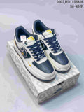 Pair of white, navy, and yellow Nike Air Force 1 low-top sneakers displayed on a patterned shoebox; style code 2607JYD1156A26 and size range 36–45 are visible.