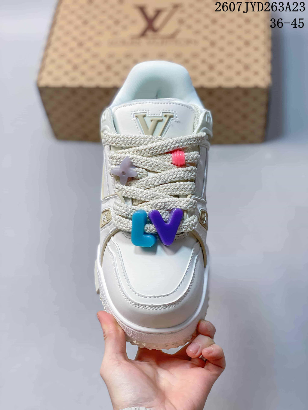 Top view of a white sneaker with braided laces, multicolor decorative charms and raised tongue branding; image text shows code 2607JYD263A23 and size range 36–45.