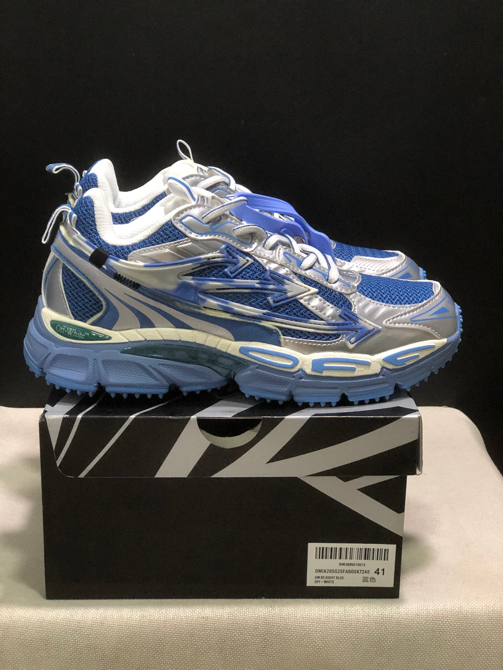 Side view of the sneakers showing layered panels, arrow detailing, and blue textured outsoles.