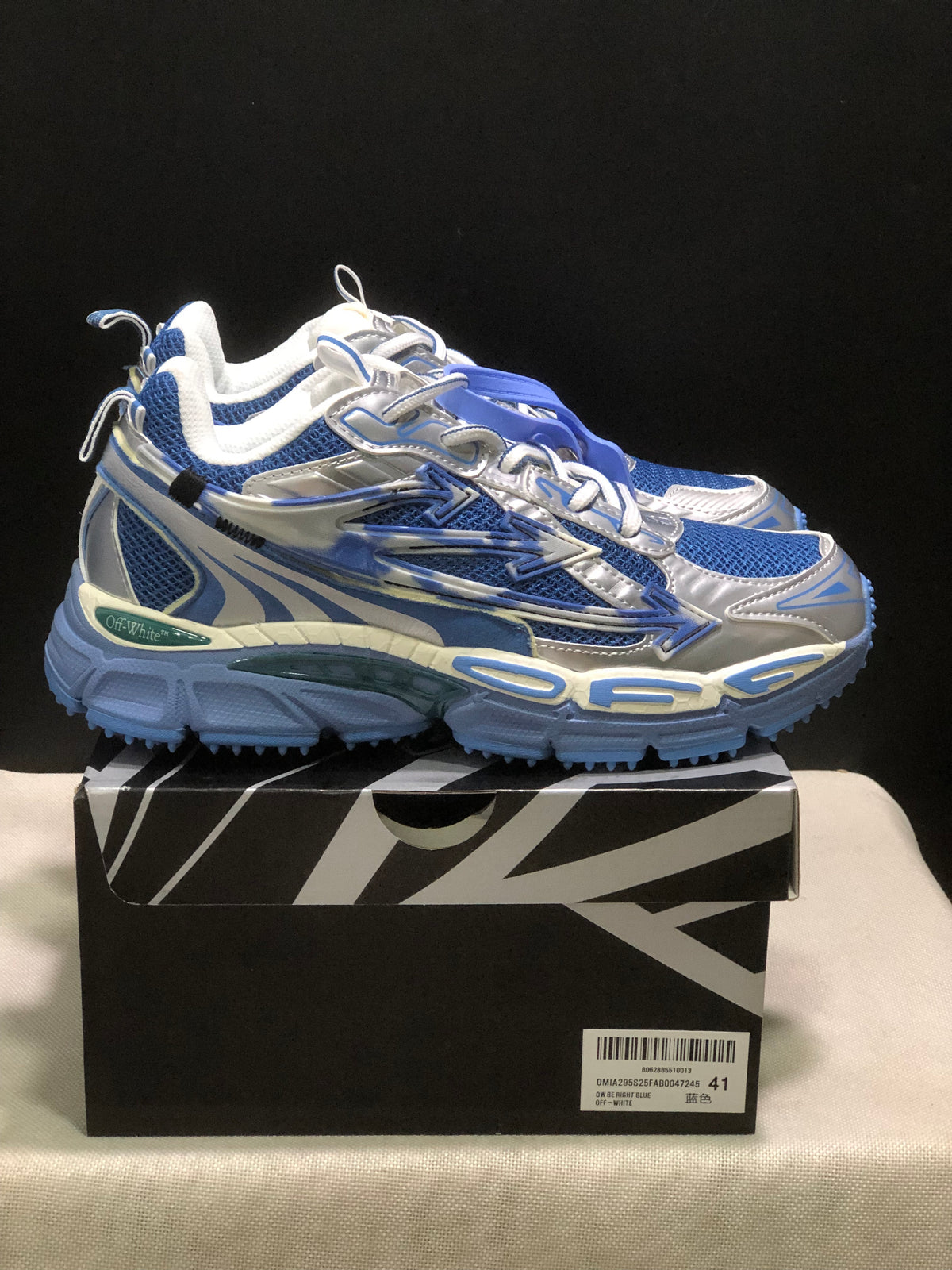 Side view of the sneakers showing layered panels, arrow detailing, and blue textured outsoles.