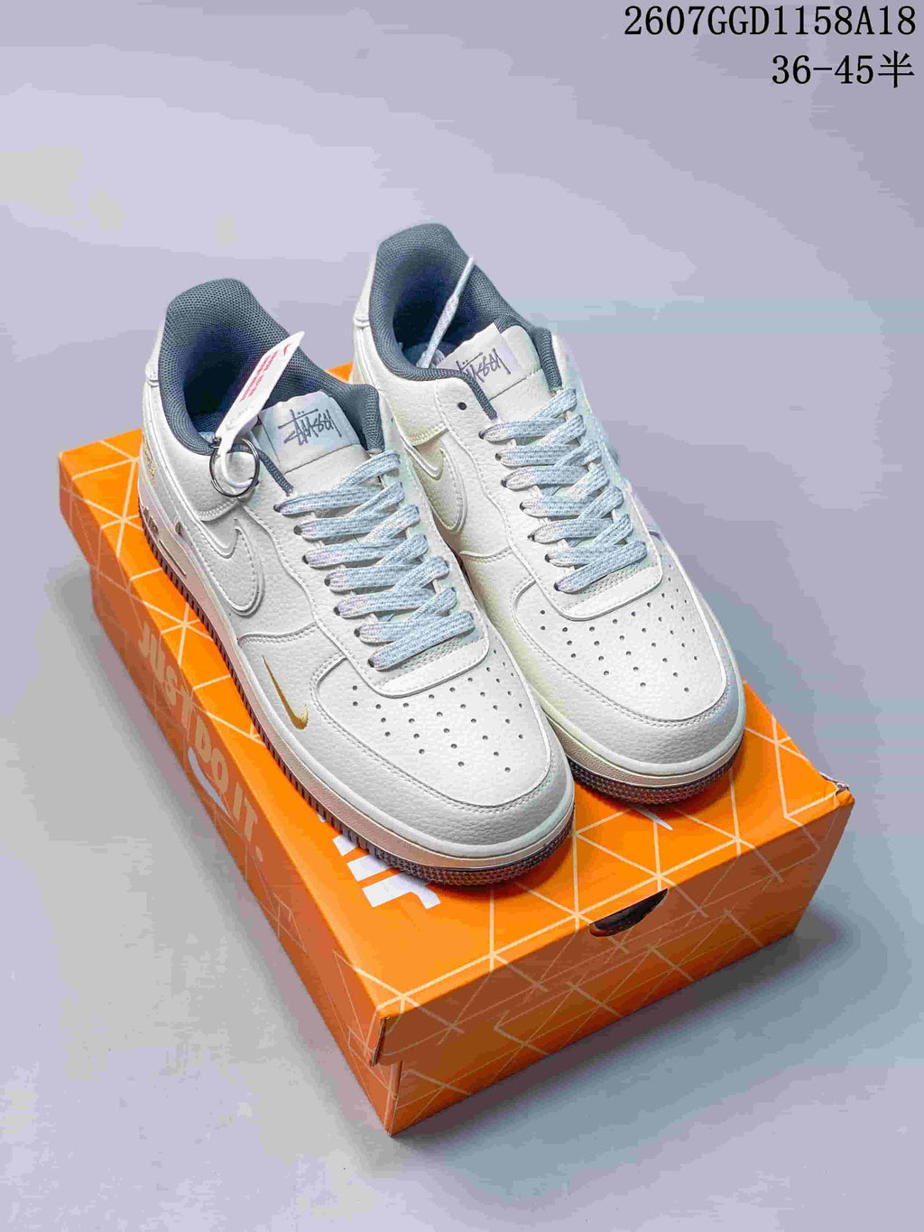 Pair of white low-top Nike sneakers with dark lining and contrasting accents displayed on an orange shoebox; style code 2607GGD1158A18 and size range 36–45 are visible.