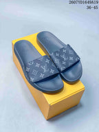 Pair of blue-gray monogram slide sandals displayed on a yellow box.
