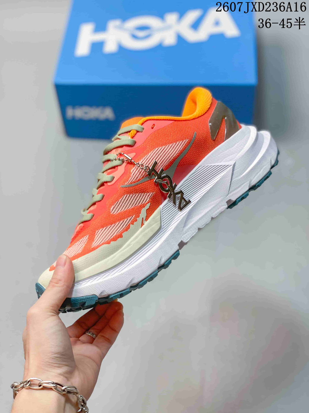 Side profile of the coral Hoka trail running shoe showing mesh panels, layered overlays, thick white sole, and dark heel detail.