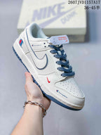 Angled side view of the white and blue low-top sneaker showing the swoosh, blue laces, red accent detail, and outsole.