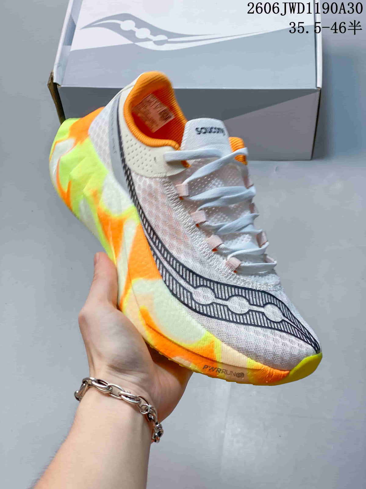 Angled side view of a white Saucony running shoe with orange and neon accents and a sculpted sole.