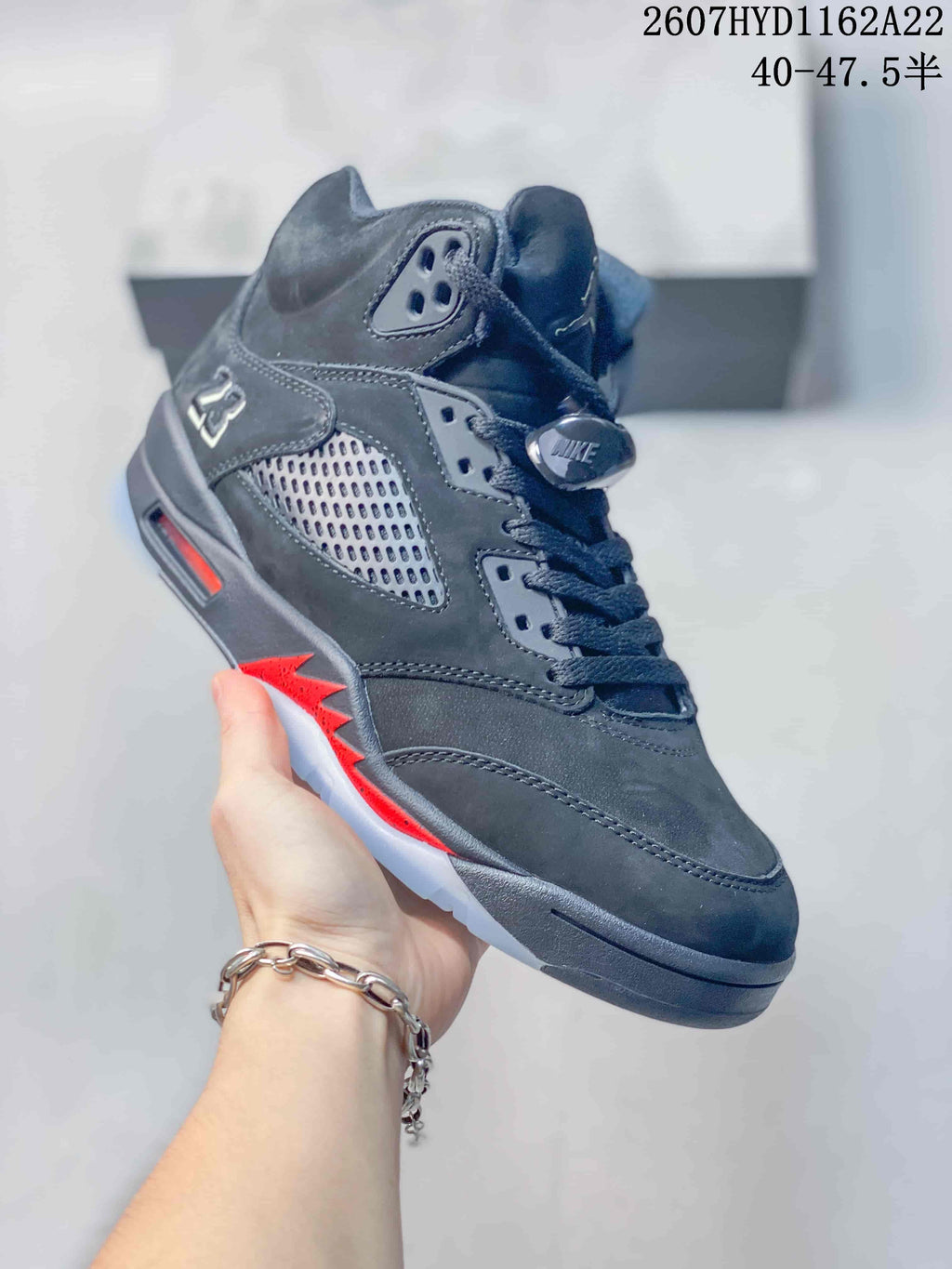 Angled side view of the black high-top sneaker showing the perforated panel, red midsole accents, gray laces and translucent outsole.