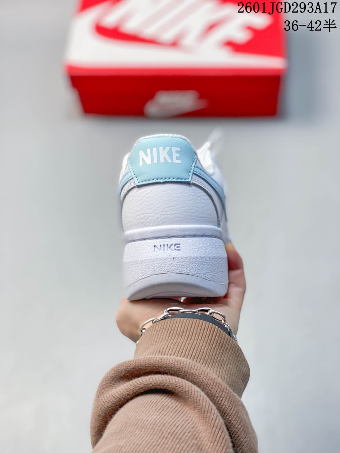 Rear view of a white Nike sneaker with a light blue heel detail and raised sole.