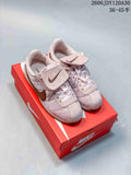 Pair of pale pink Nike Classic Cortez sneakers with brown accents and tongue flaps, shown on a red shoebox