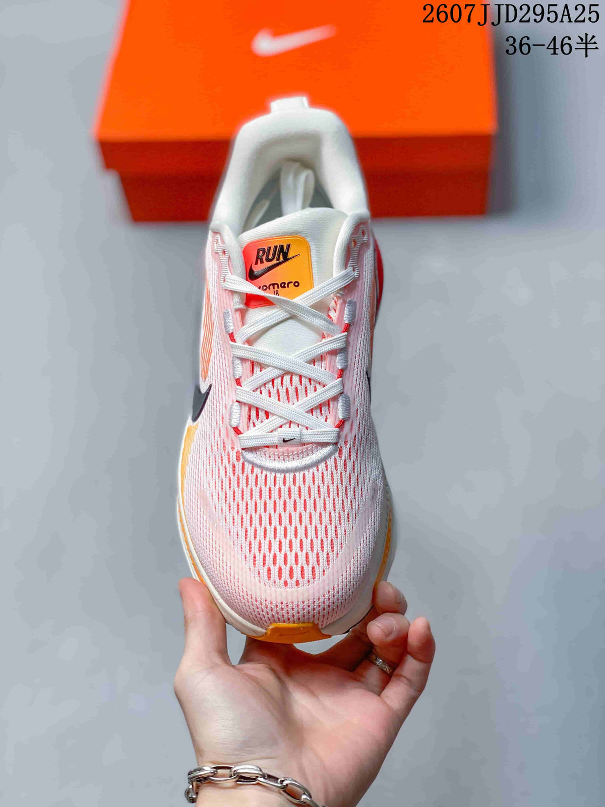 Top view of a Nike Vomero 18 sneaker showing the mesh-look pink and white upper, laces, and orange tongue label.