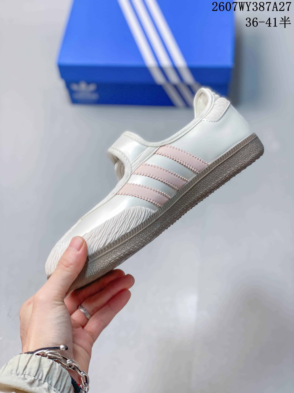 Side view showing the white upper, three soft pink stripes, textured toe detail, and gum-colored outsole.