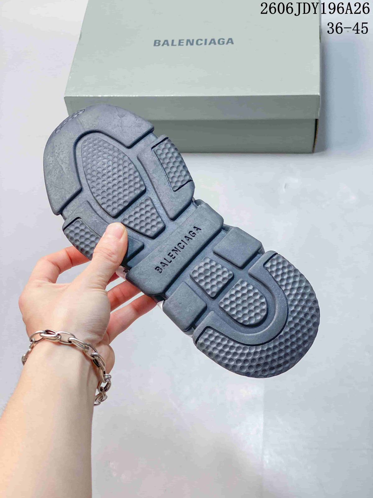 Underside of a dark gray sneaker showing the segmented textured outsole and Balenciaga branding, with the branded shoebox in the background.