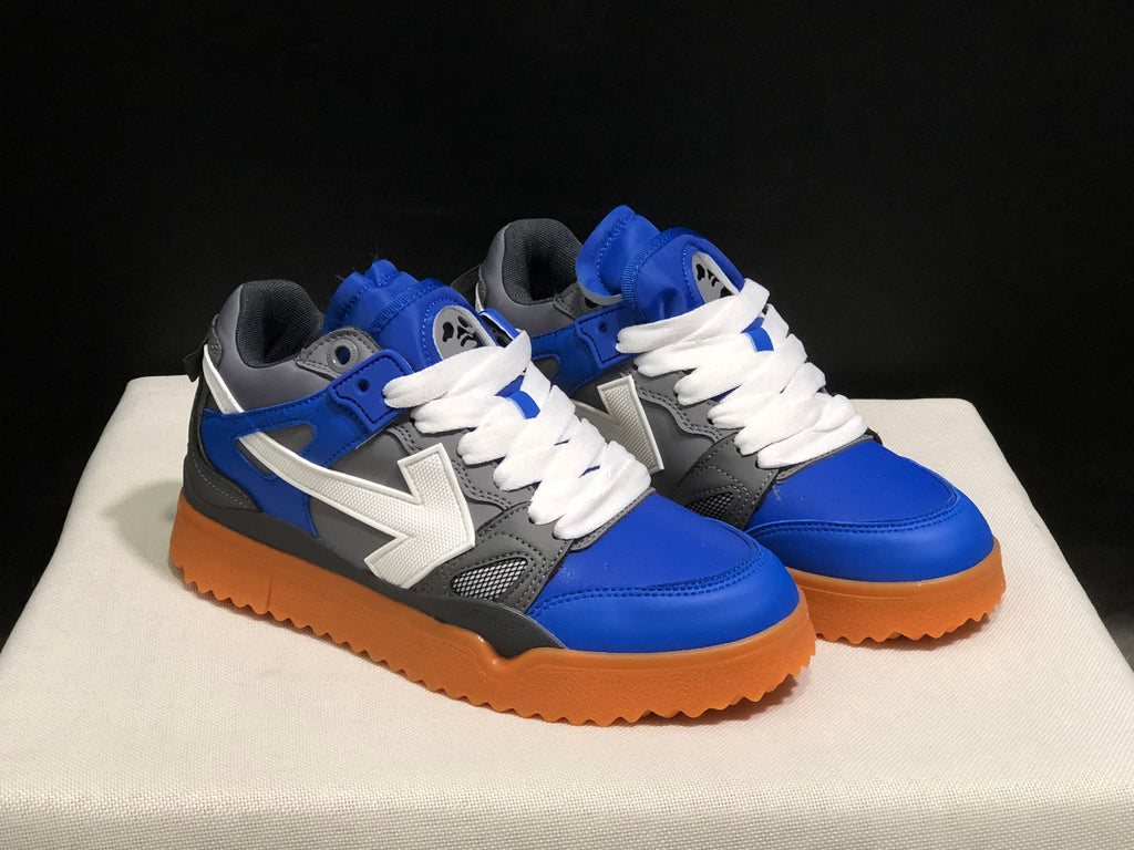 Front three-quarter view showing the blue toe boxes, white laces, grey panels, and large side arrow details.