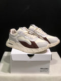 Pair of white and brown low-top sneakers displayed on a white shoebox, showing the side profile and sculpted sole.