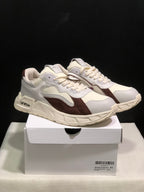 Pair of white and brown low-top sneakers displayed on a white shoebox, showing the side profile and sculpted sole.