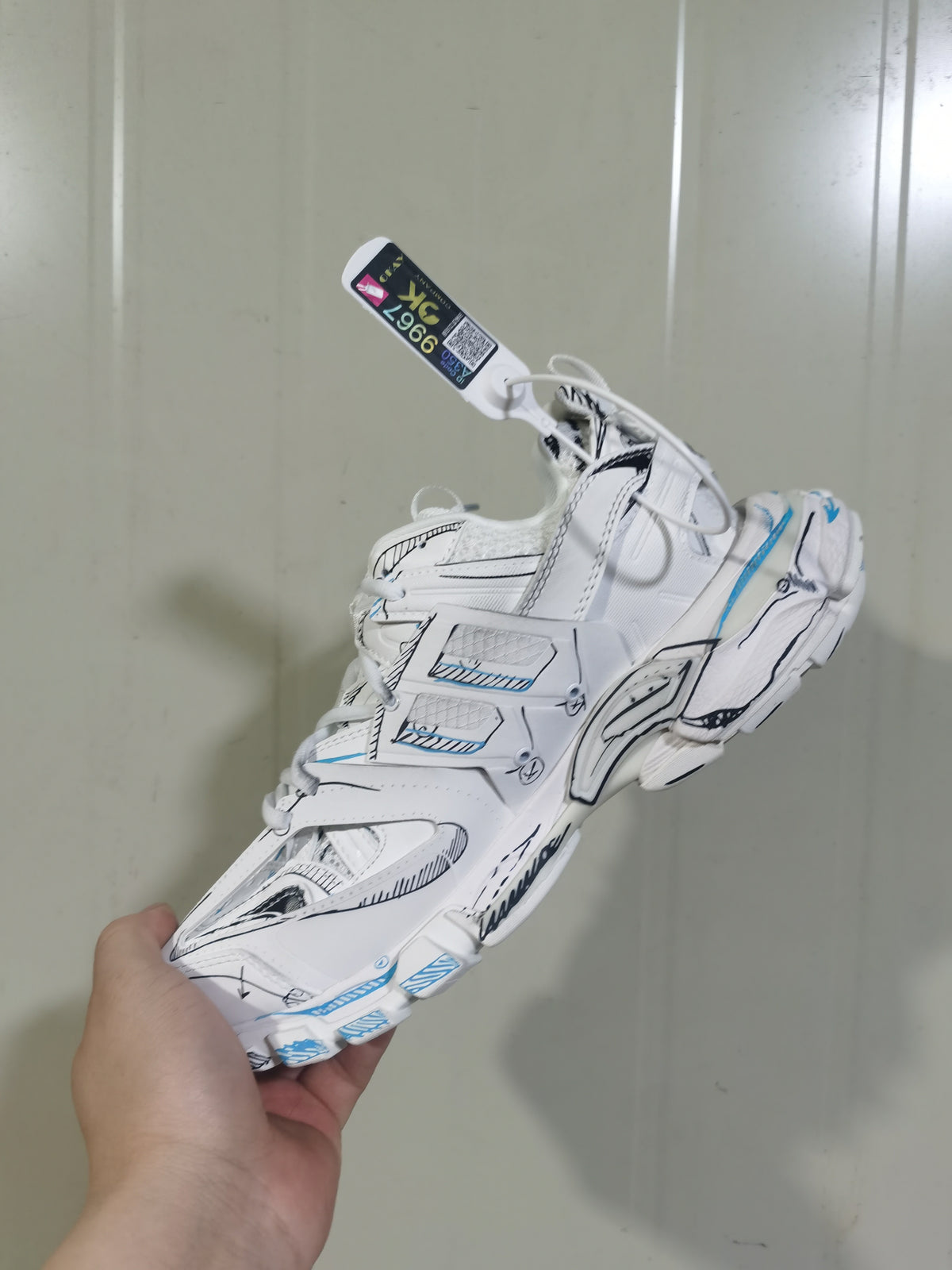 White, black, and blue track sneaker shown from an angled side view, highlighting layered panels and sculpted sole details.