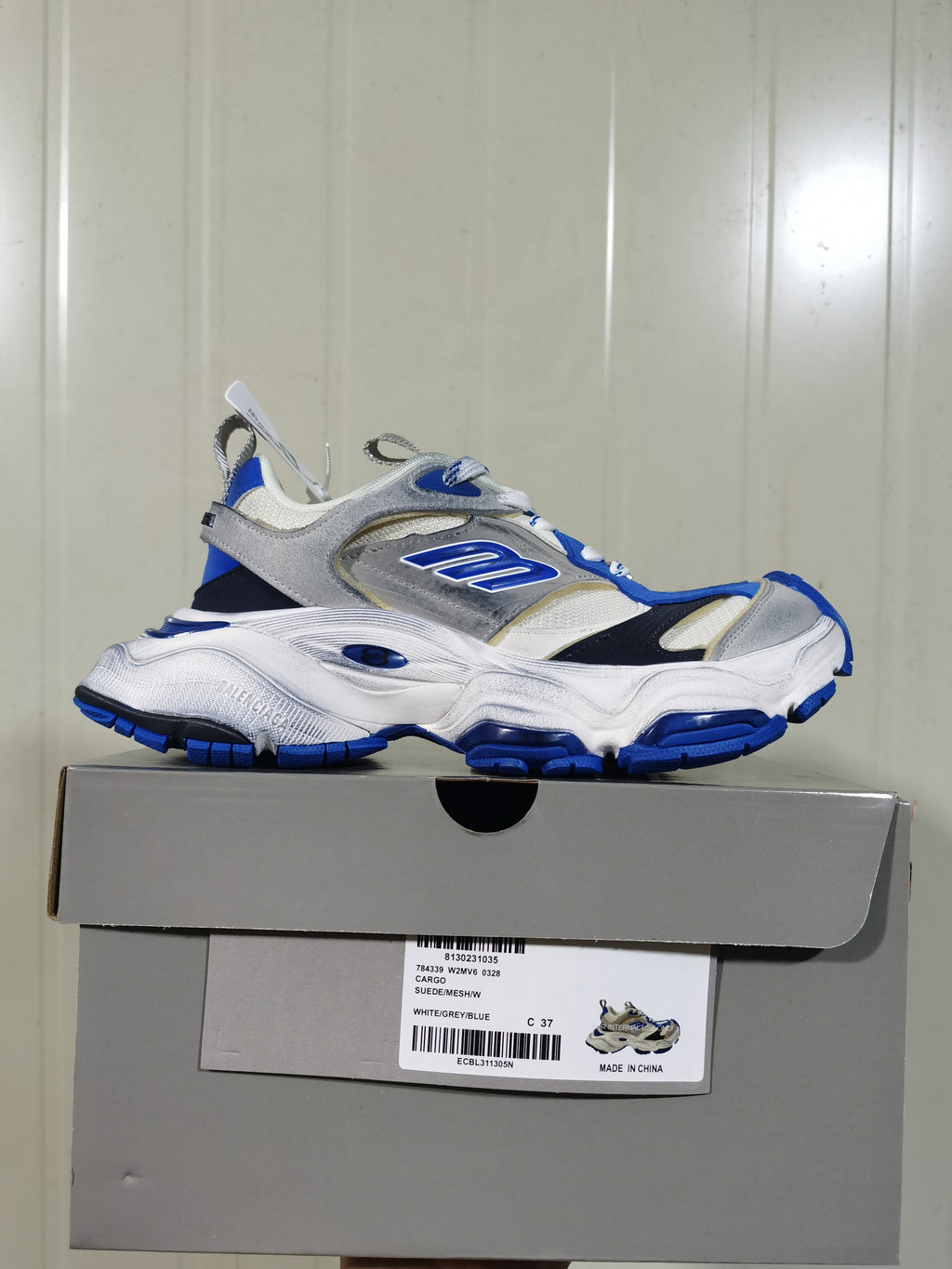 White, grey, and blue Skechers sneaker displayed on its shoebox, with the box label visible.