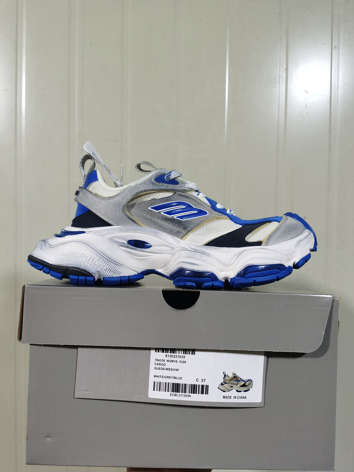 White, grey, and blue Skechers sneaker displayed on its shoebox, with the box label visible.