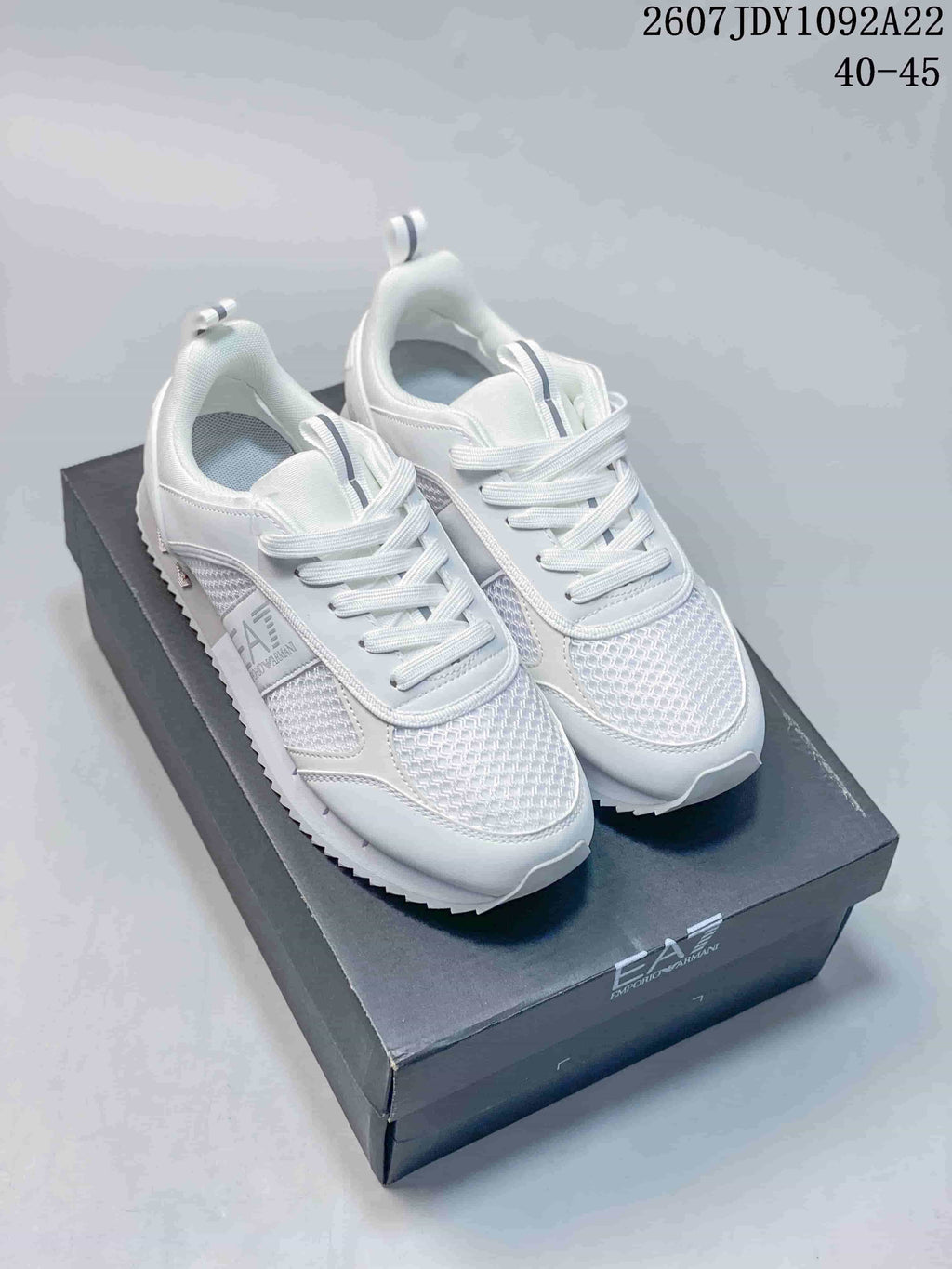 White EA7 low-top sneakers with textured toe panels, white laces and a serrated outsole displayed on a branded box.