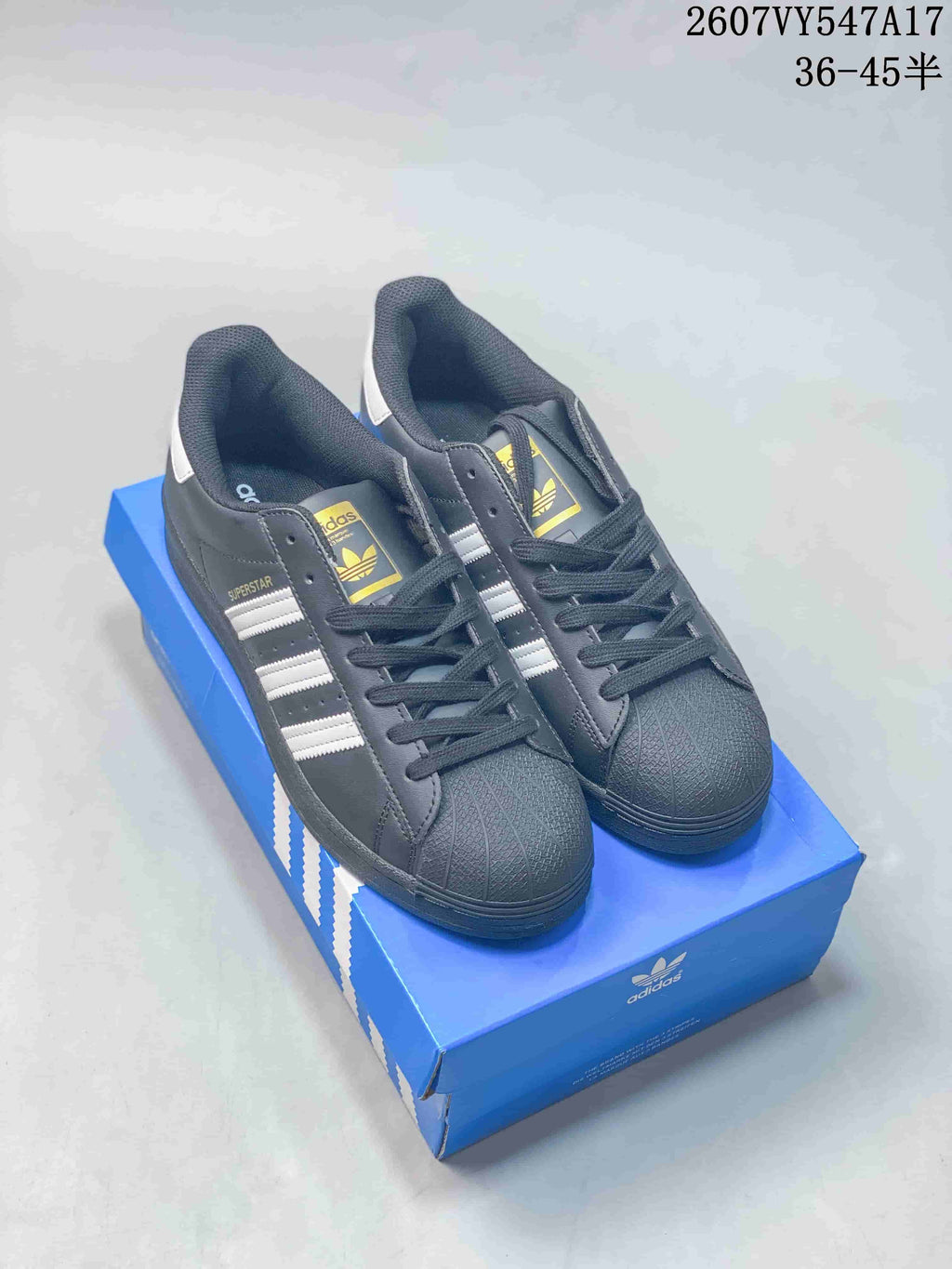 Pair of black Superstar sneakers displayed on a blue adidas shoebox with Trefoil tongue branding.