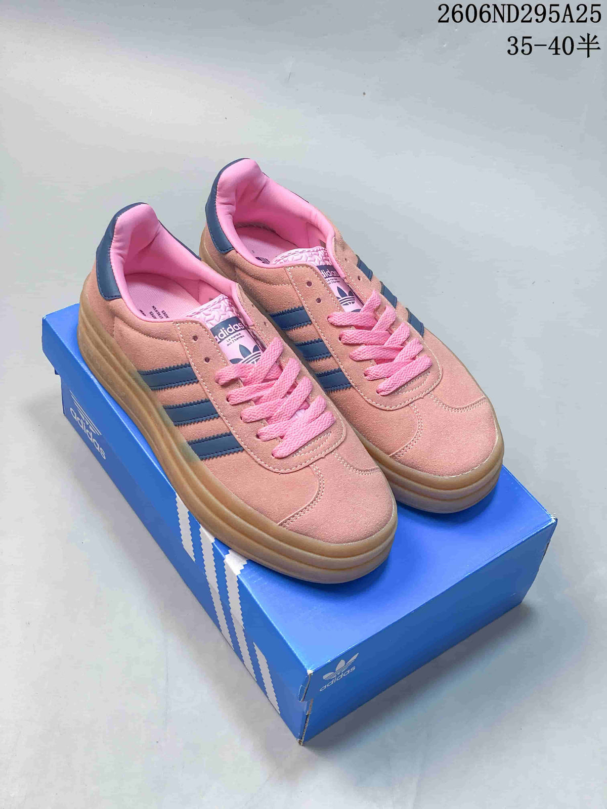 Pair of pink Adidas sneakers with navy stripes and gum platform soles displayed on a blue shoebox.