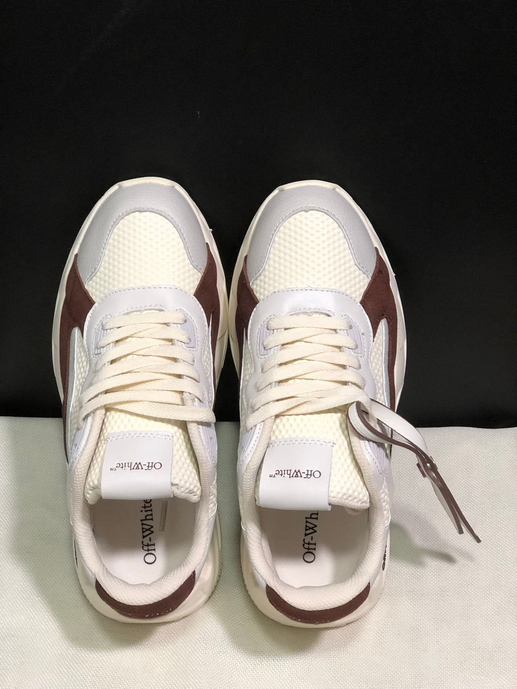 Top-down view showing the lace-up fronts, textured white panels, padded collars, and attached hangtag.