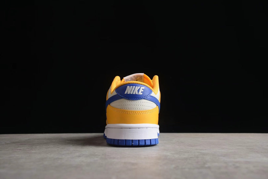 Rear view of a Nike sneaker showing the blue heel detail, white heel panel, and wheat gold lower section.