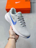 Angled side view of a light gray Nike running shoe with a blue Swoosh, white midsole, and blue outsole tip.