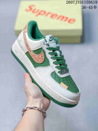 Close-up of a white and green low-top sneaker with a textured copper-colored side overlay, green laces, perforated toe box, and white midsole.