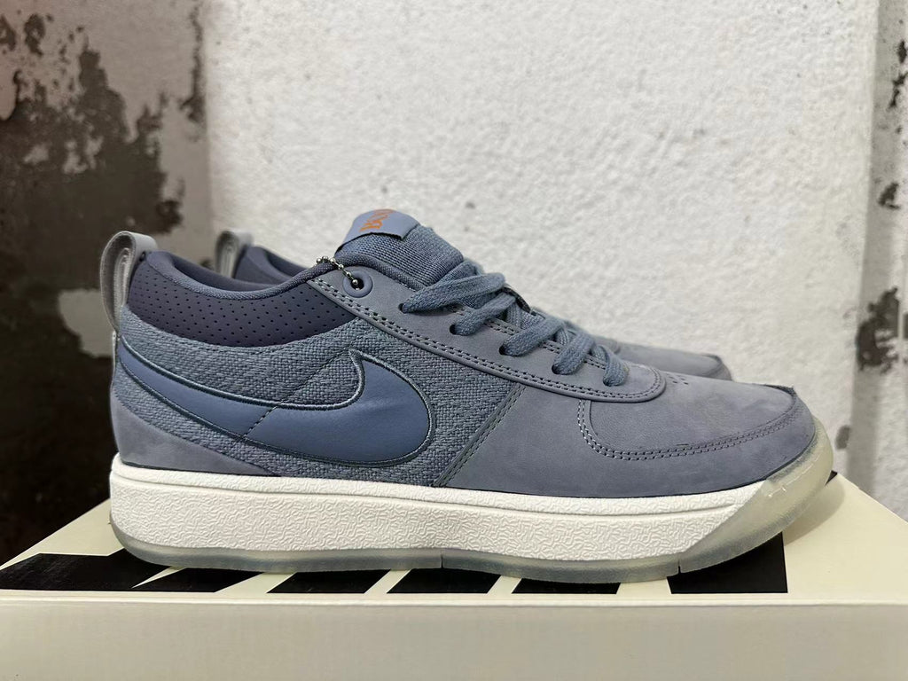 Side view of a blue-gray Nike Book 1 shoe showing the Swoosh and layered upper