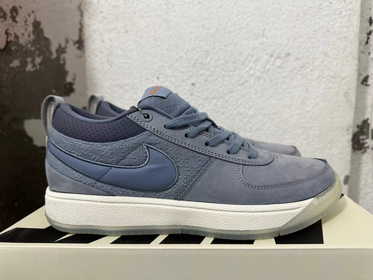 Side view of a blue-gray Nike Book 1 shoe showing the Swoosh and layered upper