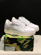 Pair of white BAPE Sta low-top sneakers with gray heel panels displayed on a camouflage shoebox.