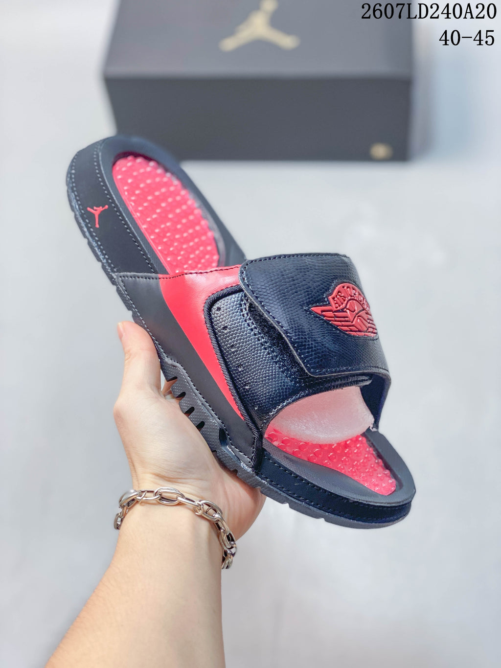 Angled view of the black and red Jordan slide showing the adjustable strap, red footbed, open toe, and outsole.