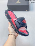 Angled view of the black and red Jordan slide showing the adjustable strap, red footbed, open toe, and outsole.