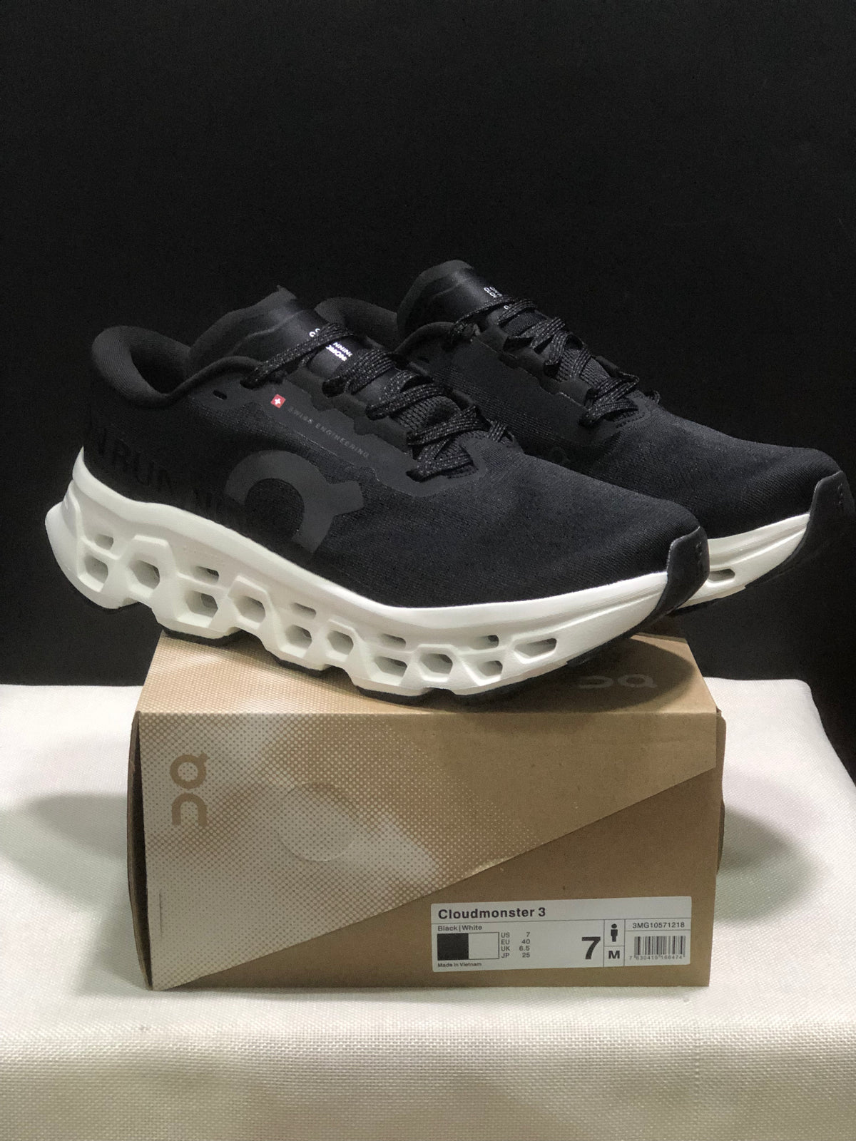 Pair of black and white On Cloudmonster 3 sneakers displayed on a branded shoe box.