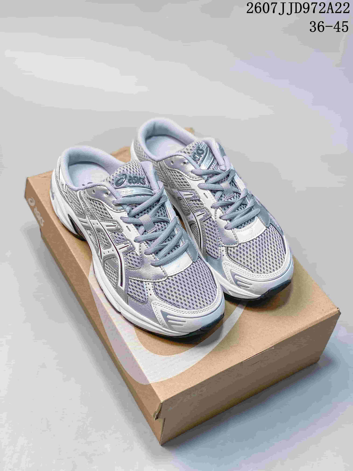 Pair of white and silver ASICS Gel-1130 sneakers displayed on a shoebox; style code 2607JJD972A22 and size range 36–45 are visible.
