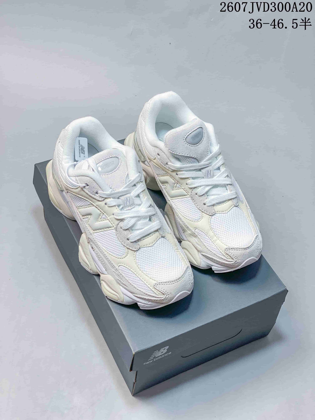 Pair of white and light cream New Balance 9060 sneakers displayed on a shoebox.