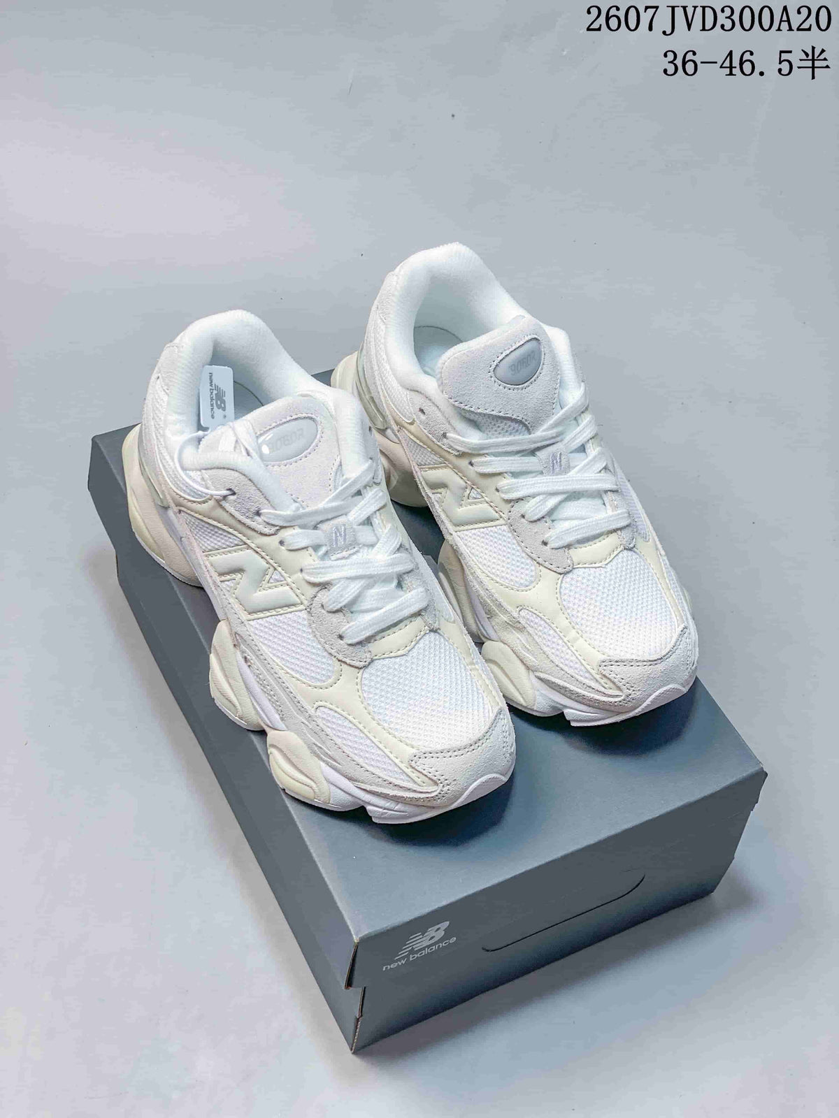 Pair of white and light cream New Balance 9060 sneakers displayed on a shoebox.