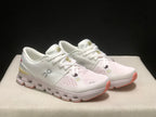 Three-quarter view of the ivory and sand shoes with white uppers and coral outsole accents.