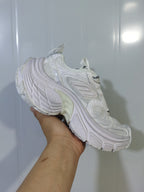 White chunky sneaker shown from the outer side, highlighting layered panels, mesh sections, and a sculpted sole.