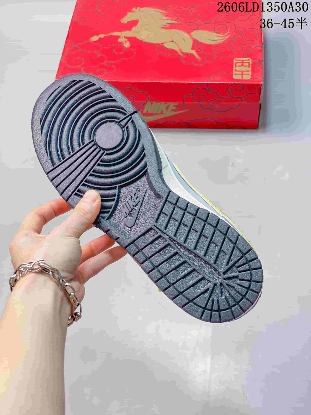 Dark outsole of the Nike SB Dunk Low sneaker beside a red horse-themed box.