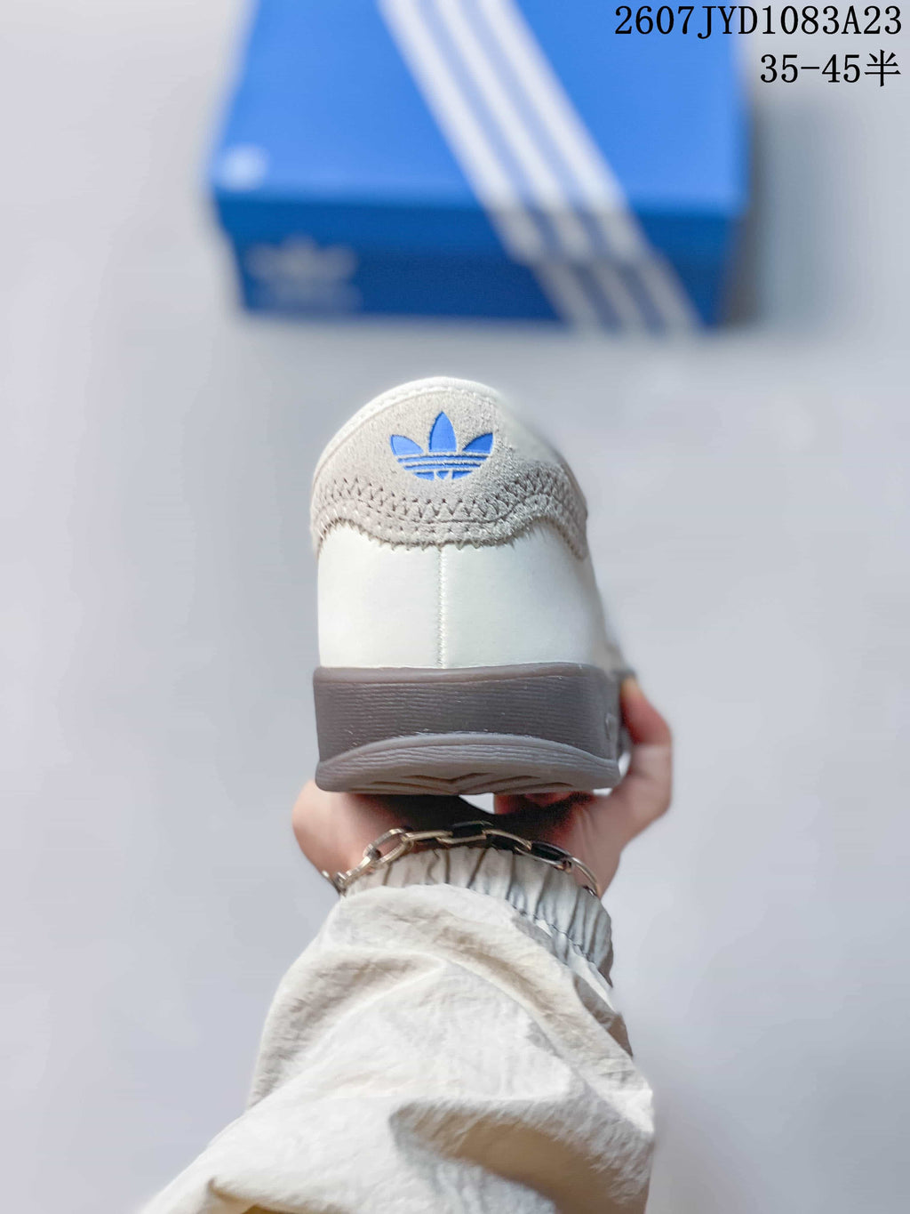 Rear view of the white sneaker showing the padded heel, blue trefoil-style branding, and dark outsole edge.