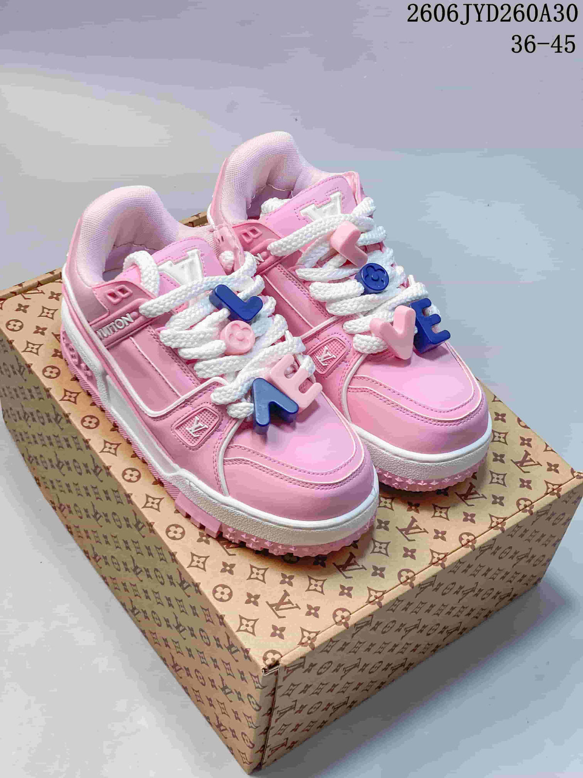 Pink Louis Vuitton Trainer Maxi sneakers with white laces and colorful charms, shown on a patterned box.